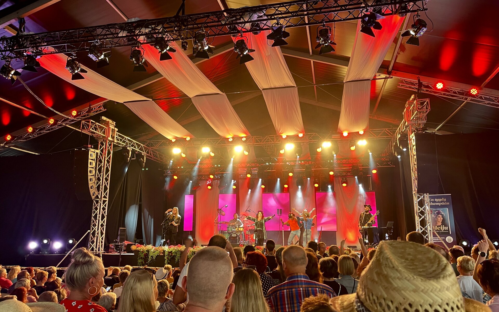Meiju Suvas live on a covered tent stage: the singer centre stage with the band, red-lit trussing and LED panels behind, crowd in the foreground